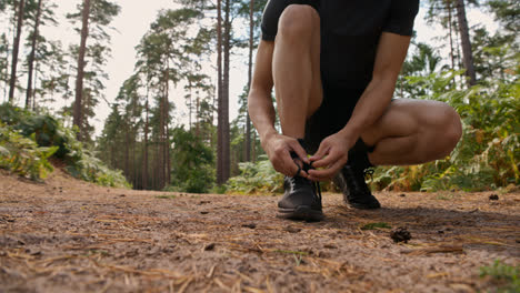 Primer-Plano-De-Un-Hombre-Atándose-Los-Cordones-De-Una-Zapatilla-Deportiva-Antes-De-Hacer-Ejercicio-Corriendo-Por-Una-Pista-A-Través-Del-Bosque,-Filmado-En-Tiempo-Real